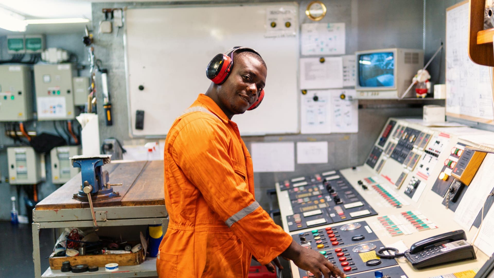 Engineer in orange coveralls and ear defenders at a power plant control panel